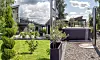 Trädgård med gräsmatta, krukor, stenläggning och modernt hus med uterum under en molnig himmel.