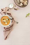 Skål med krämig tomatsoppa, brödskivor i en korg, en sked och en liten skål med salt.