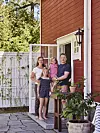 En familj står vid ytterdörren till ett rött trähus med vita detaljer och stenlagd uteplats.
