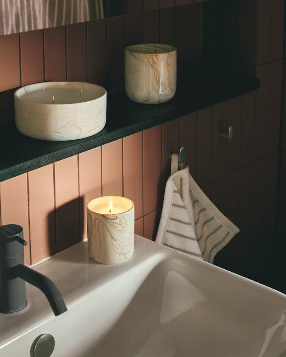 Handfat i ett badrum med tändt ljus, handduk och två keramiska burkar på en mörk hylla.