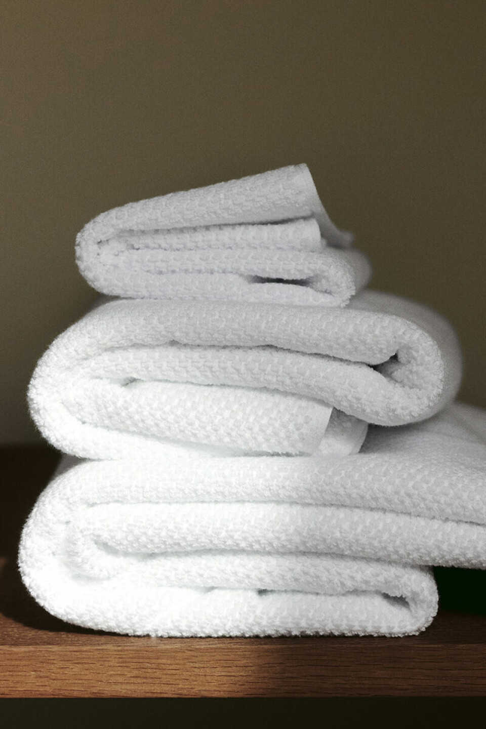 Staplar av vikta vita handdukar ligger på en träyta mot en mörk bakgrund.