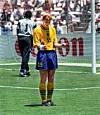Fotbollsspelare i gul tröja nummer 19 står på gräsmattan framför mål och gestikulerar med händerna.