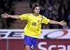 Fotbollsspelare i gul tröja och blå shorts springer med armarna utsträckta.