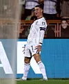 Fotbollsspelare i vit dräkt firar med armarna utåt på planen.