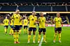 Fem svenska fotbollsspelare i gula tröjor firar på en fotbollsplan framför läktare.