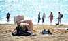 En person ligger på sanden och läser en bok på en strand med flera badgäster i bakgrunden.