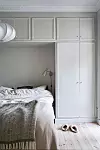 Ett ljust sovrum med obäddad säng, gardinfri vägg, inbyggda garderober och ett par tofflor på golvet.