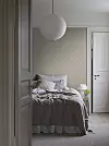 Ett sovrum med obäddad säng, rund papperslampa och ljusa väggar samt ett litet sidobord.