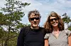 Två personer står utomhus framför träd och klippor under en klar himmel.