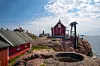 Röd byggnad och fyr på klippor vid havet under en ljus molnig himmel.
