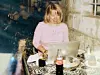 En kvinna sitter vid ett bord med laptop, Coca-Cola-flaska och dryckesglas i en kafémiljö.