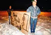 Två personer står utomhus i snö och håller upp en protestskylt med en tecknad figur.