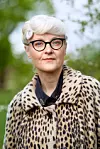 En kvinna med ljus hårstyl och glasögon bär en leopardmönstrad rock utomhus.