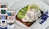 Öppet smörrebröd med fiskesallad på tallrik, intill staplade mejeriförpackningar från Arla.