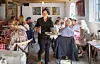 En serveringsperson går genom en restaurang med sittande lunchgäster, träbjälkar och konst på väggarna.