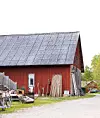 Röd lada med lutande tak, loppisprylar och möbler uppställda utanför vid en grusväg.