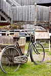 Svart cykel framför träkärl och ett plankstaket på en gårdsplan.