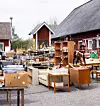 Utomhusloppis med möbler, lådor, lampor och andra second hand-varor på en grusad gårdsplan.