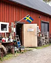 Rött trähus med öppen dörr, svensk flagga och en handskriven skylt med texten öppet.