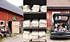 Röd lada med loppisprylar utanför, staplade textilier i hyllor och en öppen bil baklucka fylld med föremål.