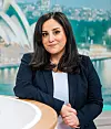 En kvinna sitter vid ett runt bord i en tv-studio med blå bakgrund och stadsvy.