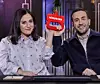 Två personer sitter i en studio och håller upp en röd statyett med texten NODROOMS.