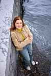 En kvinna står lutad mot en kajkant vid vattnet med armarna i kors.