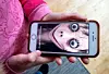 En hand håller en smartphone som visar ett ansikte med stora ögon och mörk bakgrund.