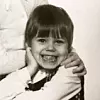 Svartvitt foto av ett leende barn med kort mörkt hår som hålls om av en vuxen.