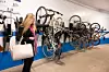 En kvinna med handväska står framför flera cyklar som hänger längs en vägg i ett garage.