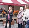 Tre kvinnor står på kullersten utanför en uteservering med röd markis i Gamla stan.