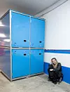 En kvinna sitter hukad på golvet bredvid ett stort blått skåp i ett garage.
