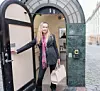 Kvinna i svart klädsel står i en öppen dörröppning bredvid en grön kaklad vägg.