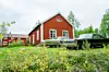 Två klassiska amerikanska bilar står på en gräsbevuxen gårdsplan framför röda trähus.