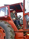 En person sitter i förarhytten på en röd traktor med stora däck.