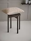En mörk träpall med en ljus, fluffig kudde står framför en ljus vägg.