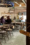 Människor sitter vid bord i ett kafé med trästolar, grönt golv och en skylt där det står Café.