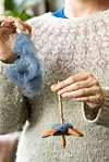 Person som spinner blå ull med en handhållen spinnrock i ett nära beskuret porträtt.