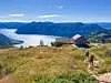 Två vandrare går längs en stig på en grön sluttning med utsikt över fjorden och bergen.