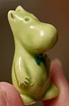 En liten grön keramikfigur formad som Mumin hålls mellan tumme och finger.