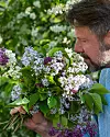 En man i profil håller en färgrik bukett med lila och vita blommor mot en grön bakgrund.
