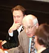 Två män sitter vid ett konferensbord, den ena i mörk kostym och den andra i ljus kavaj.