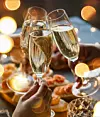Tre champagneglas hålls upp framför ett bord med tilltugg.