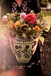 En stor keramisk vas med blå dekor fylld av färgglada blommor hålls framför en mörk klänning.