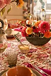 Ett dukat bord med blommig duk, en skål med färska blommor och glas samt porslin i varma färger.