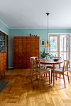 Matrum med teakbord, fyra stolar, stort vitrinskåp och ljusgröna väggar intill fönster.