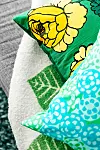 Närbild av staplade prydnadskuddar med blommiga och grafiska mönster i grönt, turkost och vitt.