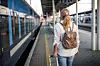En person med ryggsäck står på en tågstationsperrong bredvid ett tåg.
