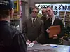 Tre män i en butik, två bakom en disk och en i förgrunden med ryggen mot kameran.