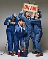 Fyra personer i blå overaller i studio med en ”ON AIR”-skylt och mikrofon.